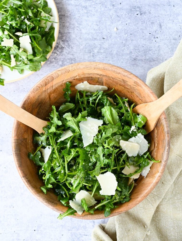 Utensils in a wooden bowl of arugula salad with lemon, olive oil, and Parmigiano-Reggiano. 