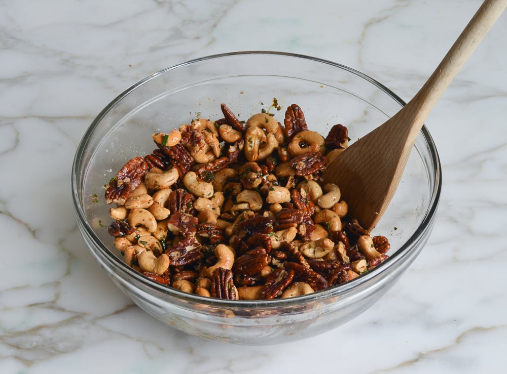 Wooden spoon in a bowl of rosemary nuts.