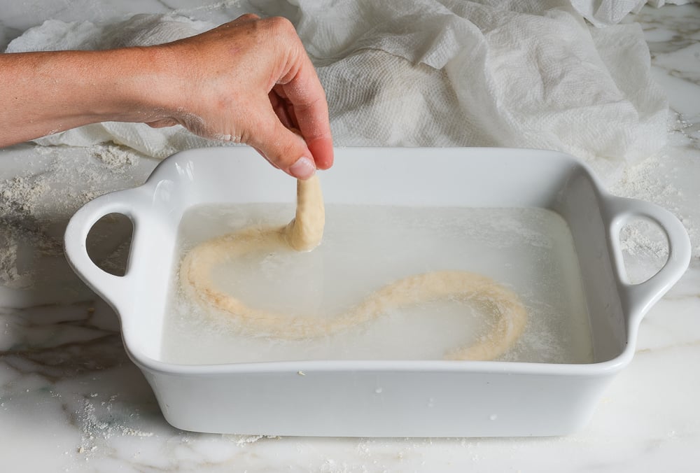 dipping soft pretzel dough into baking soda solution