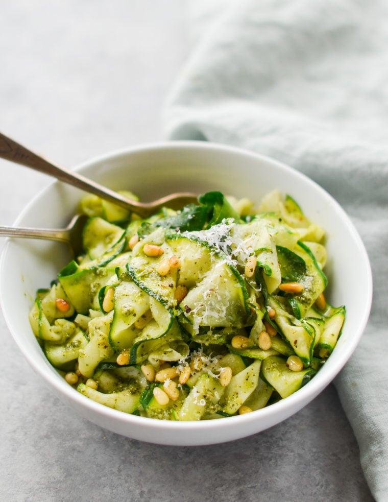 Bowl of zucchini noodles with pesto and pine nuts.