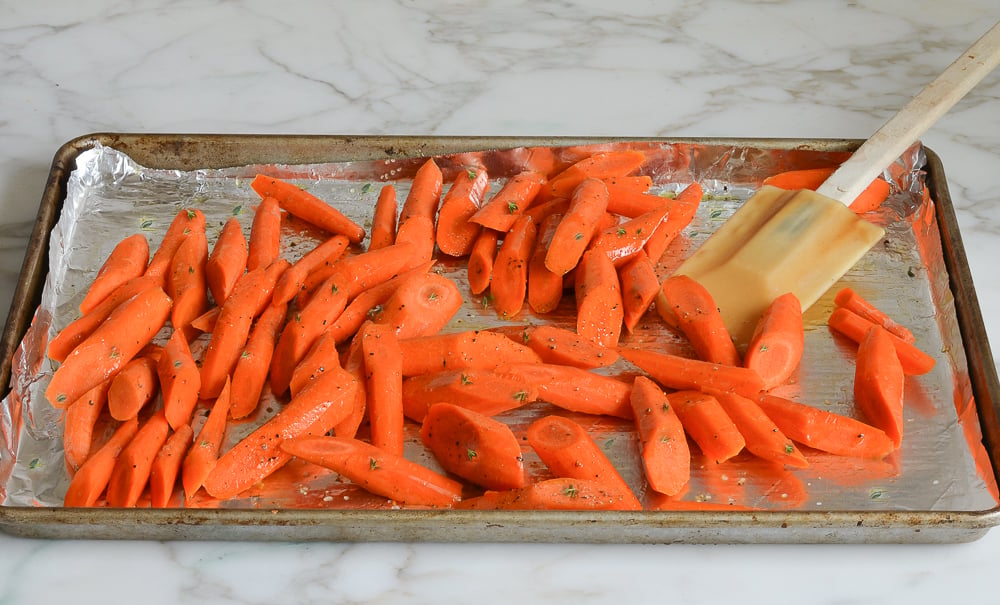 tossing carrots with oil and seasoning on baking sheet