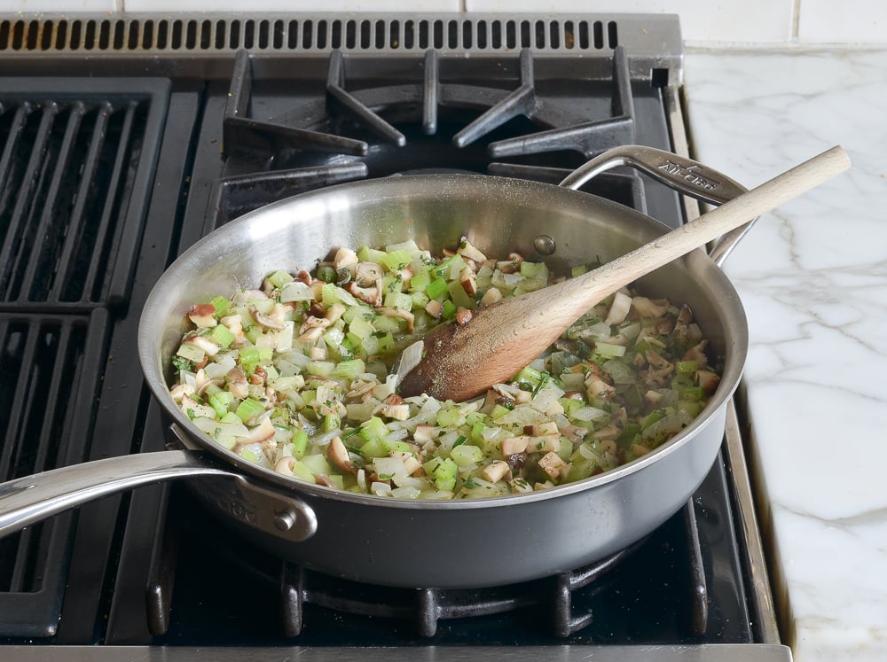 Mushrooms, herbs, and other ingredients mixed in a skillet.