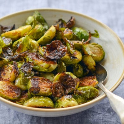 Spoon in a bowl of roasted brussels sprouts with balsamic vinegar and honey.