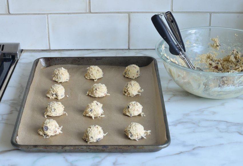 Scoops of chocolate chip cookie dough on a lined baking sheet.