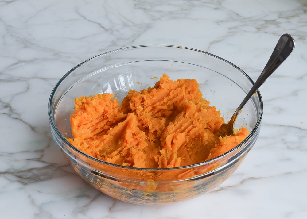 Fork mashing sweet potato in a bowl.