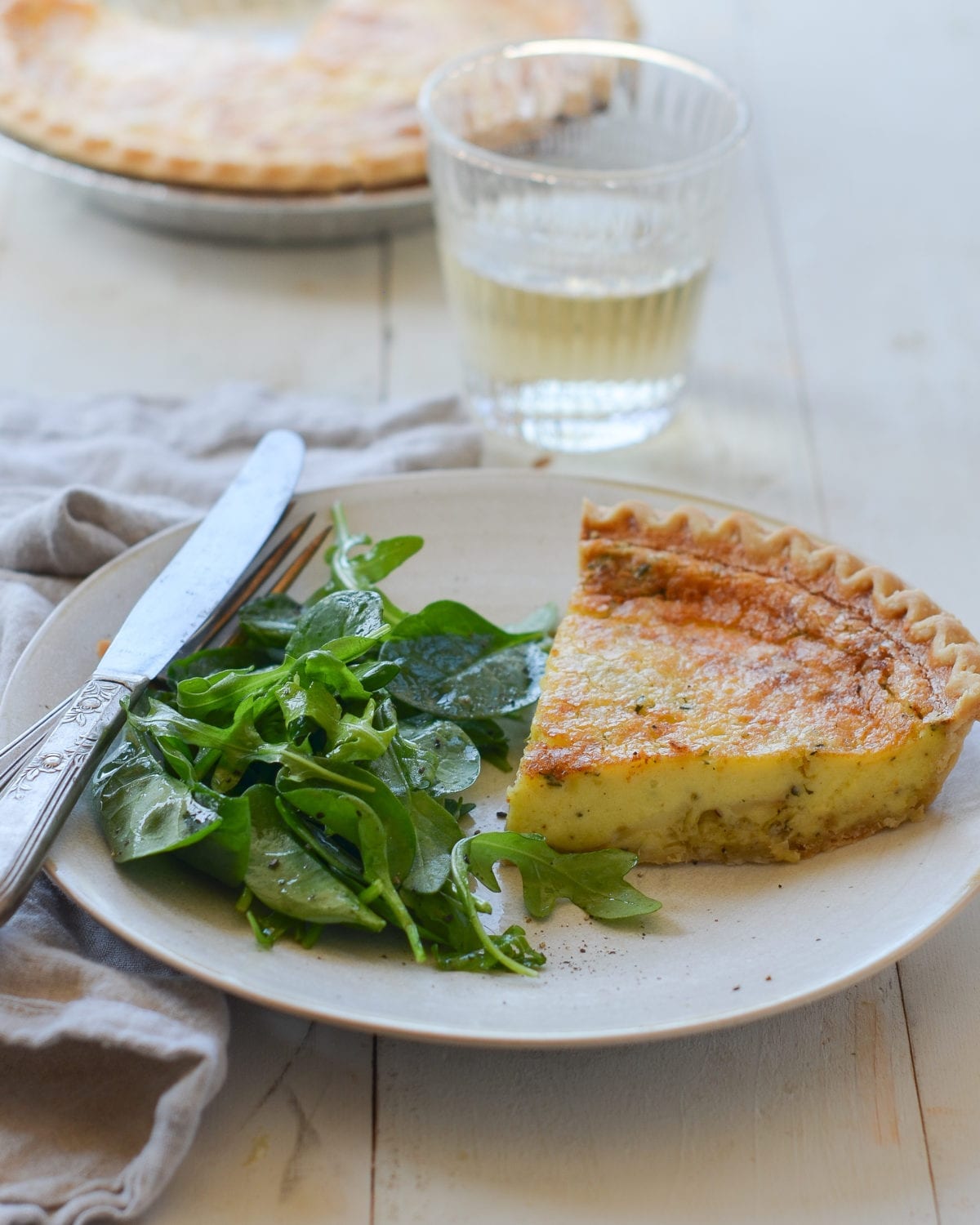 Slice of parmesan and leek quiche on a plate with greens.