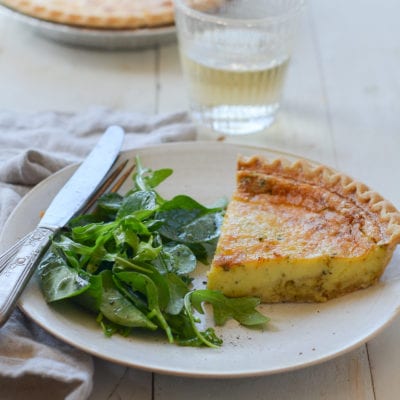 Slice of parmesan and leek quiche on a plate with greens.