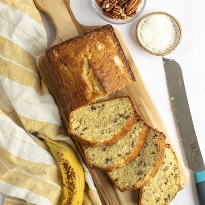 banana bread with coconut and pecans on cutting board with plaid yellow cloth