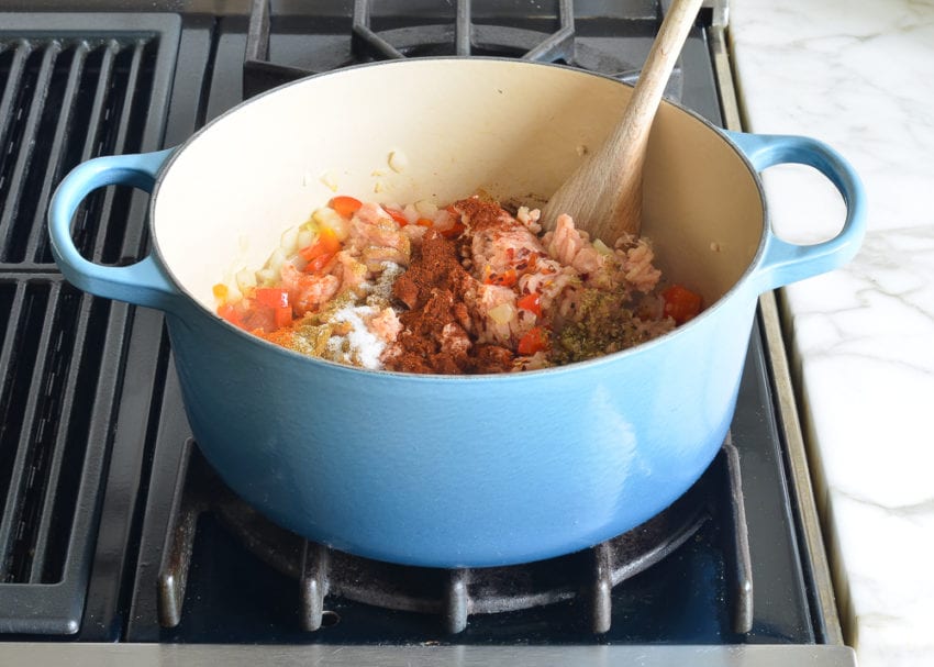Ground chicken and spices in a Dutch oven with vegetables.