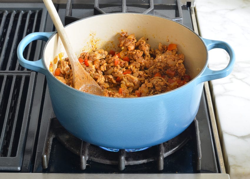 Wooden spoon in a Dutch oven with a chicken mixture.
