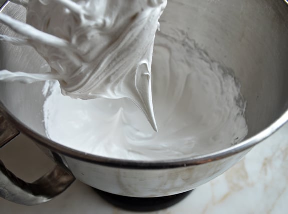 Stiff white peak of egg and sugar on the whisk of a stand mixer.