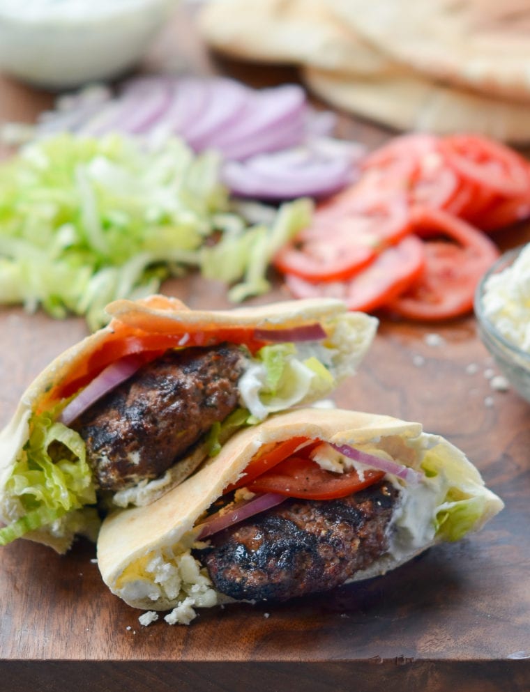 Two Greek lamb burgers on a wooden surface.
