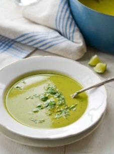 Spoon in a bowl of pea soup with basil.