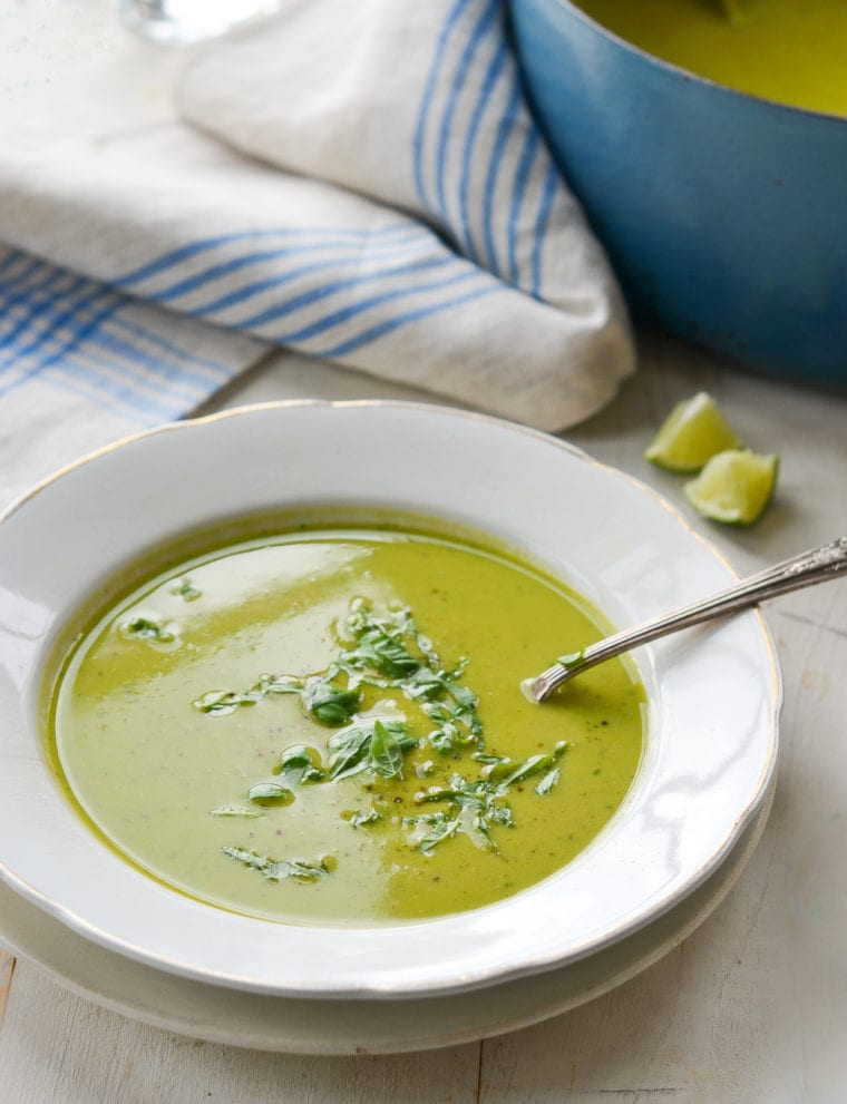 Spoon in a bowl of pea soup with basil.