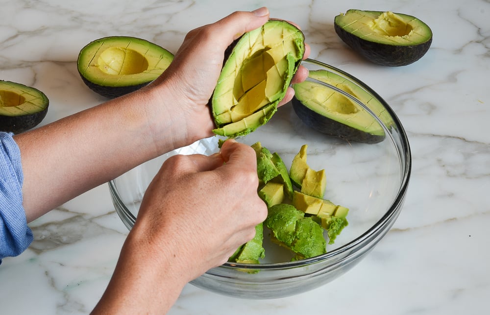 scooping avocado flesh into bowl