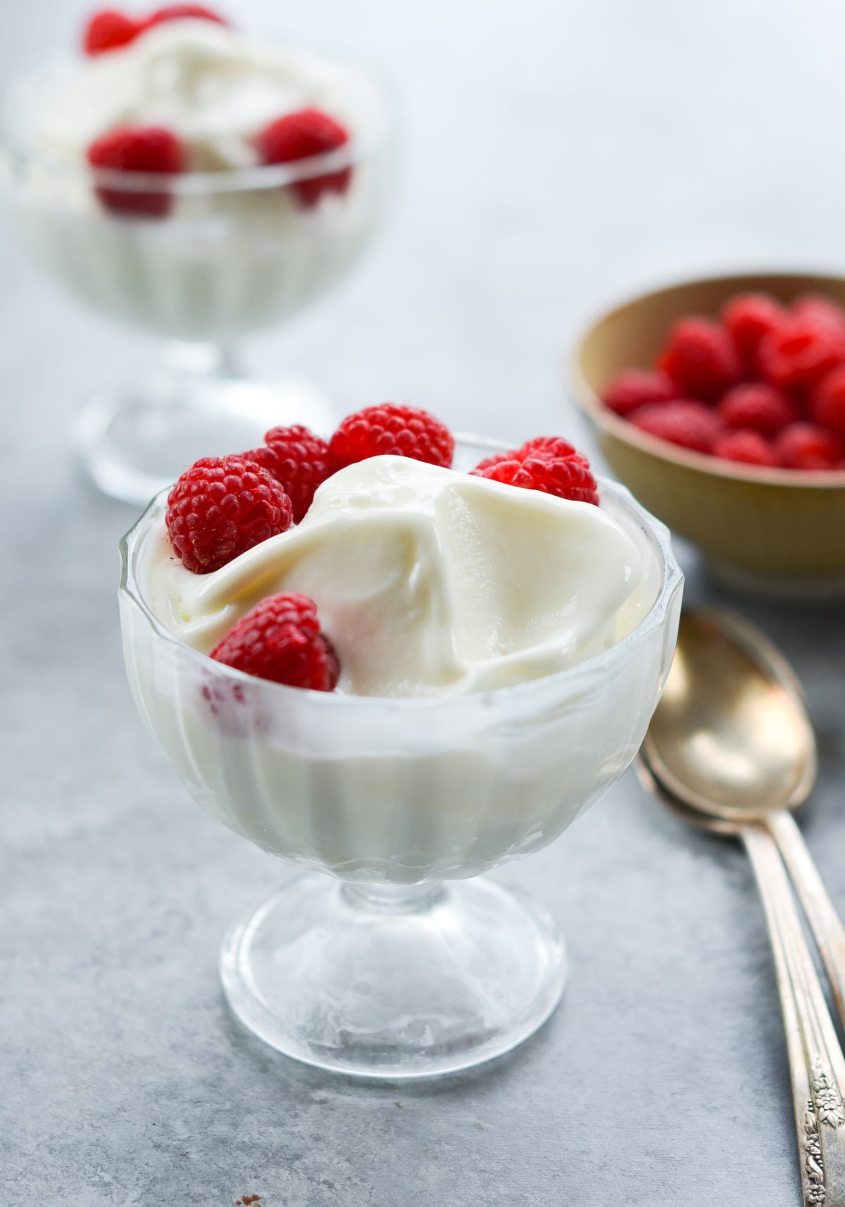 Stemmed glass of frozen yogurt topped with raspberries.