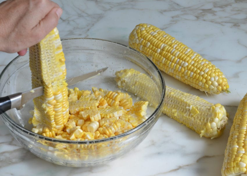 Person cutting corn kernels from a cob.