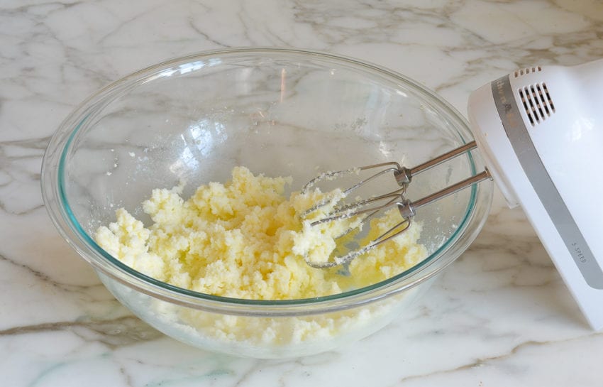 Electric mixer with a bowl of beaten butter and sugar.