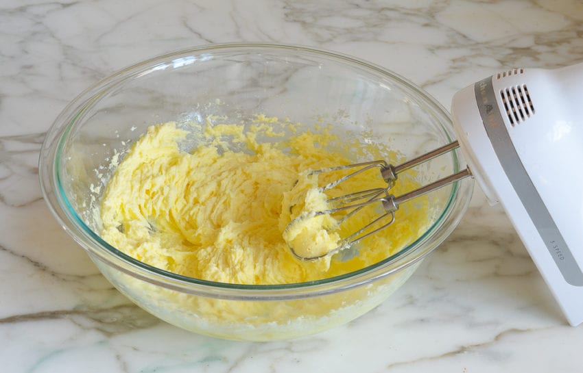 Electric mixer in a bowl with a yellow mixture.