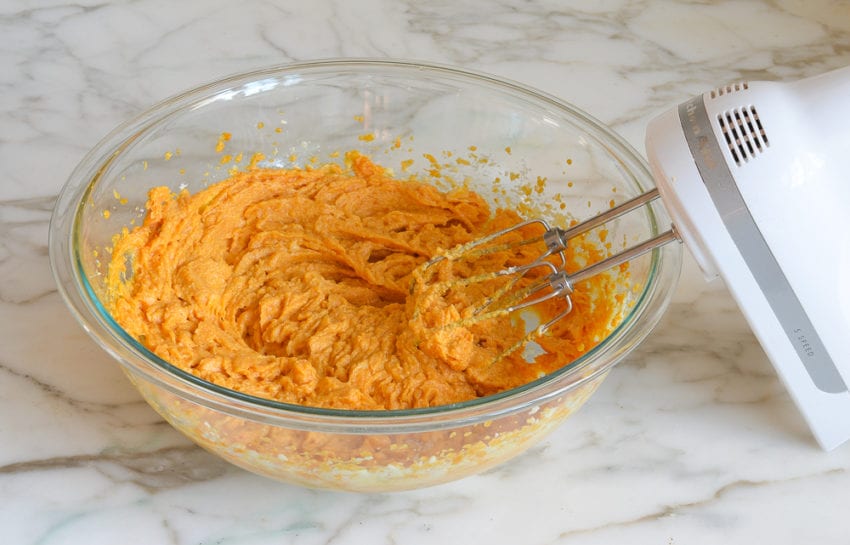 Orange mixture in a bowl with an electric mixer.