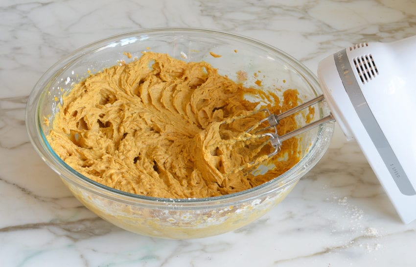 Electric mixer in a bowl with pumpkin muffin batter.
