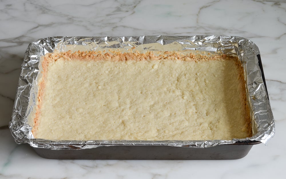 Lined baking dish with baked crust ready for lemon bar filling.