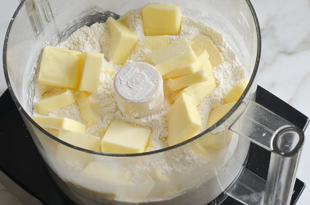 Butter cut into pieces added to a food processor with flour.
