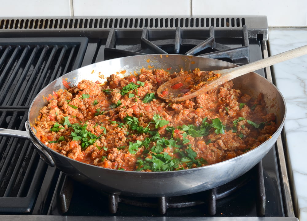 Cilantro in a skillet with ground chicken.