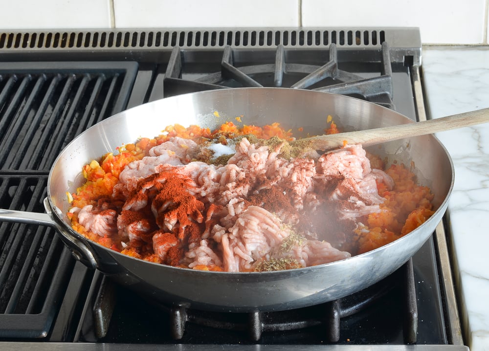 Ground chicken and spices in a skillet with vegetables.