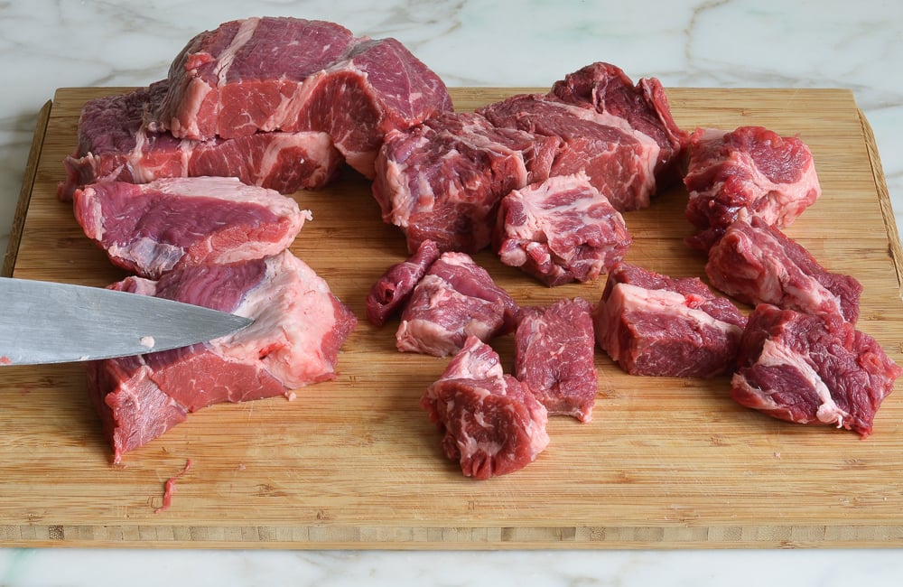 Knife cutting beef on a cutting board.