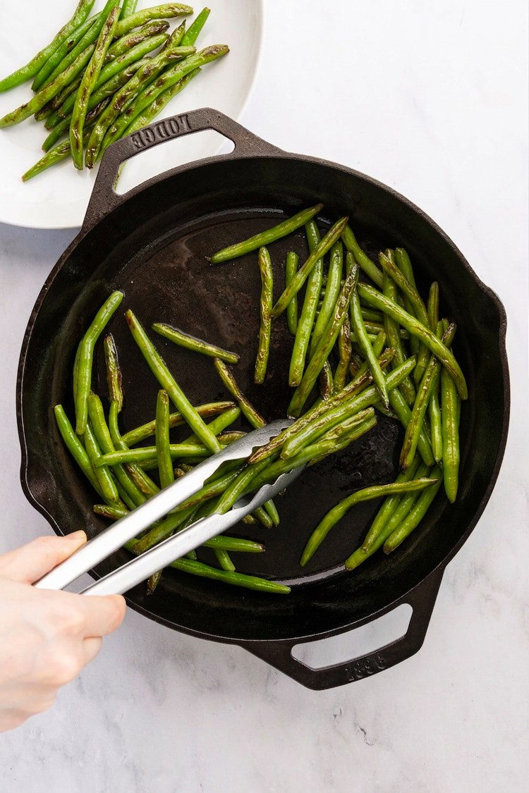 Using tongs to transfer cooked green beans from skillet to plate