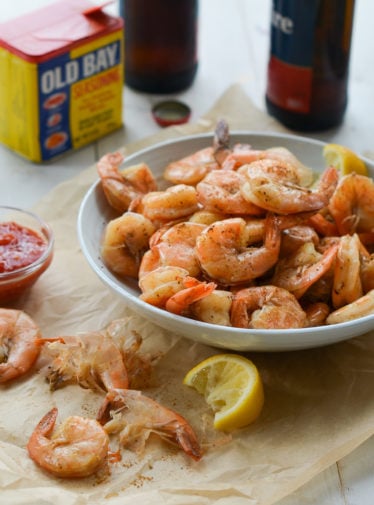 Bowl of peel-and-eat boiled shrimp with cocktail sauce in from of Old Bay Seasoning.