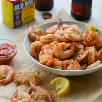 Bowl of peel-and-eat boiled shrimp with cocktail sauce in from of Old Bay Seasoning.