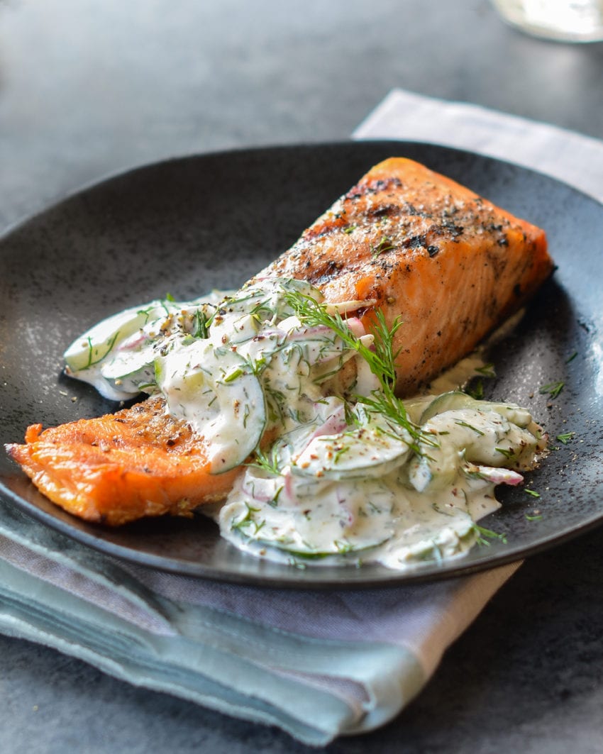 Grilled salmon on a plate with a creamy cucumber-dill salad.