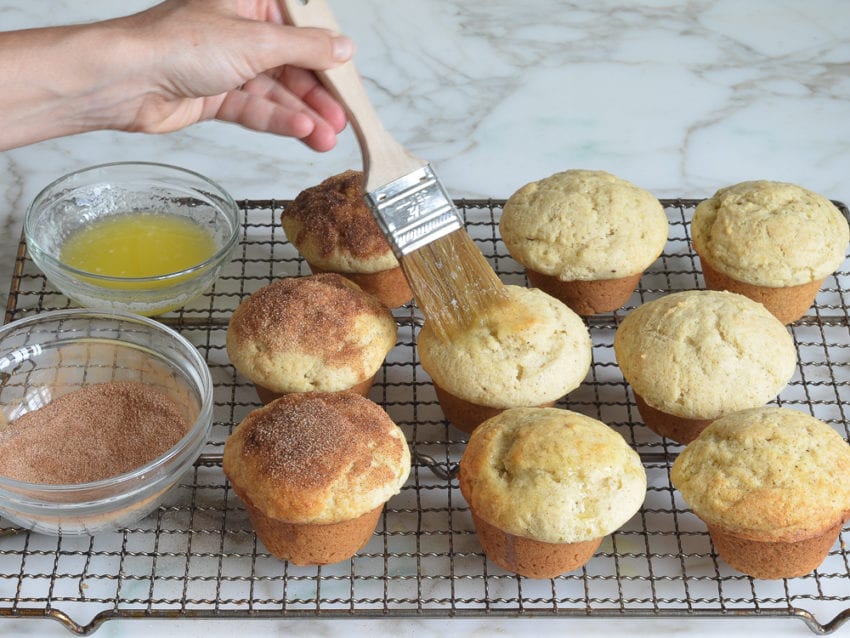 Person brushing doughnut muffins with melted butter.