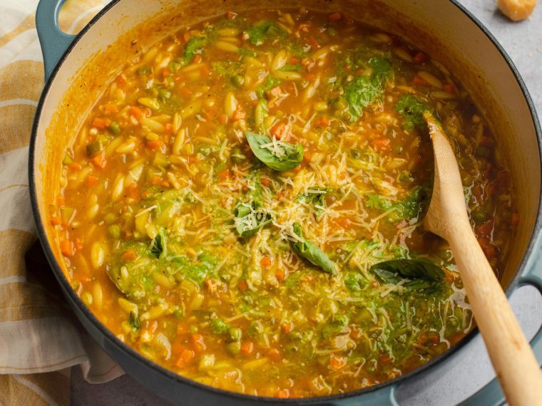 Spoon stirring a pot of summer vegetable soup.