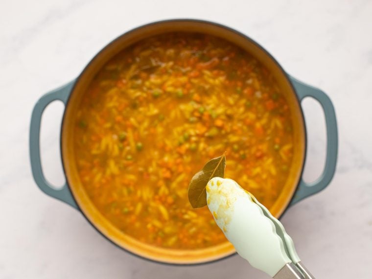 Tongs grabbing a bay leaf from a pot of vegetable soup.