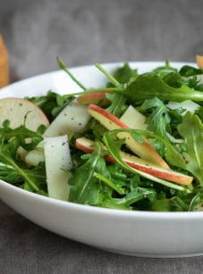 Bowl of arugula salad with apples and manchego in cider vinaigrette.