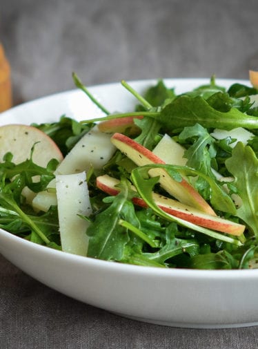 Bowl of arugula salad with apples and manchego in cider vinaigrette.