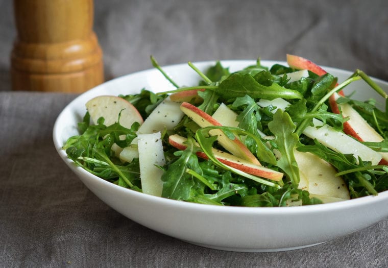 Bowl of arugula salad with apples and manchego in cider vinaigrette.