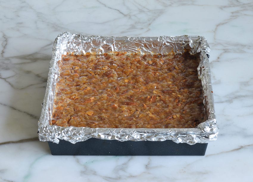 Caramel-colored pecan mixture in a foil-lined baking sheet.