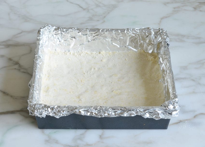 Pressed layer of flour and butter mixture in a foil-lined pan.