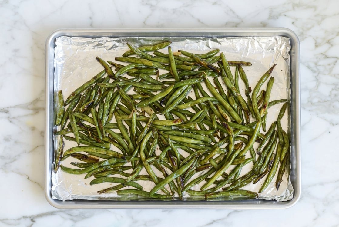 Partially roasted green beans on baking sheet.