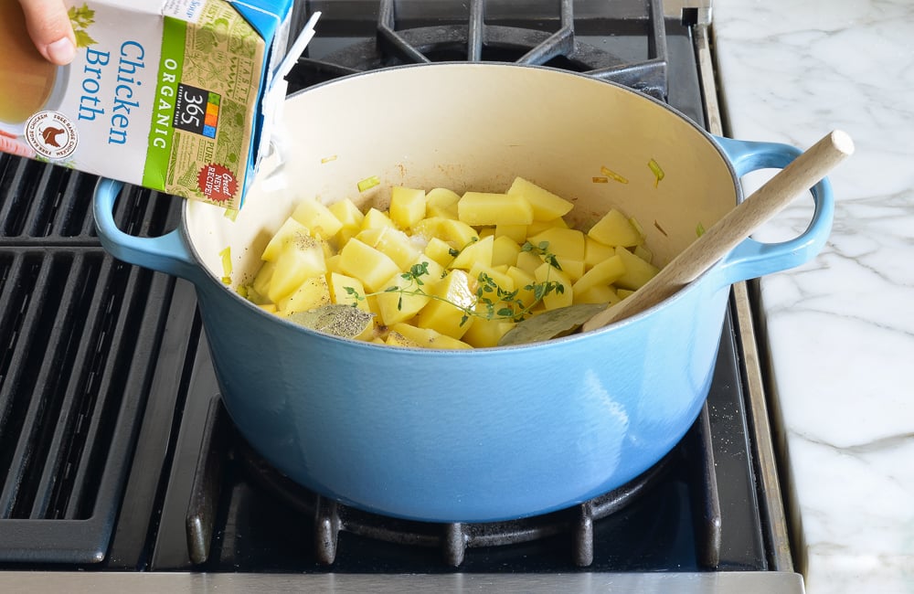 Broth pouring into a Dutch oven with leeks and potatoes.