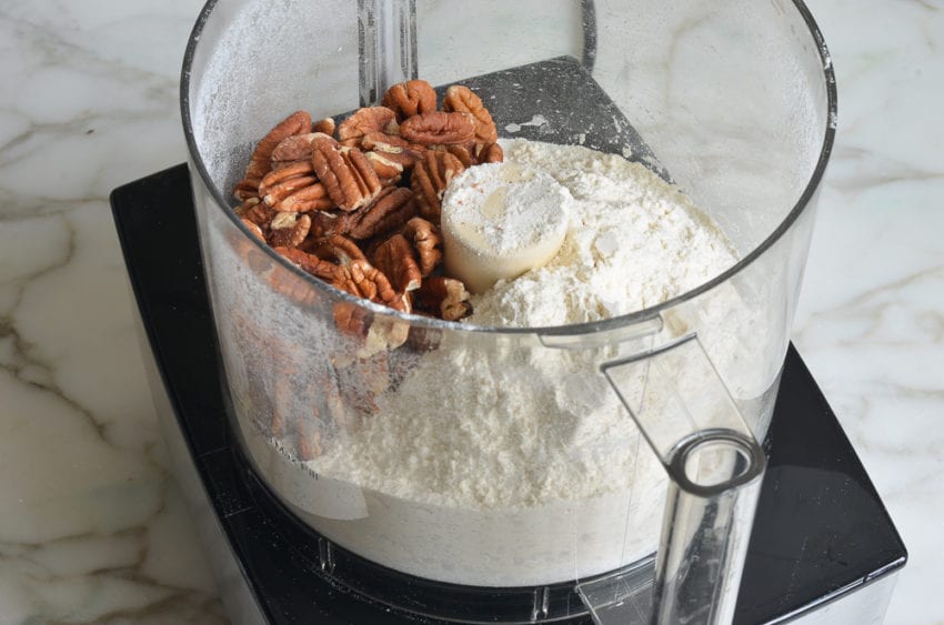 Pecans in a food processor with dry ingredients.
