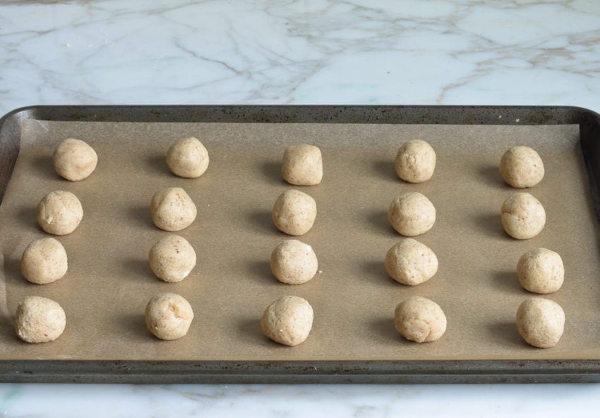 Balls of cookie dough on a lined baking sheet.