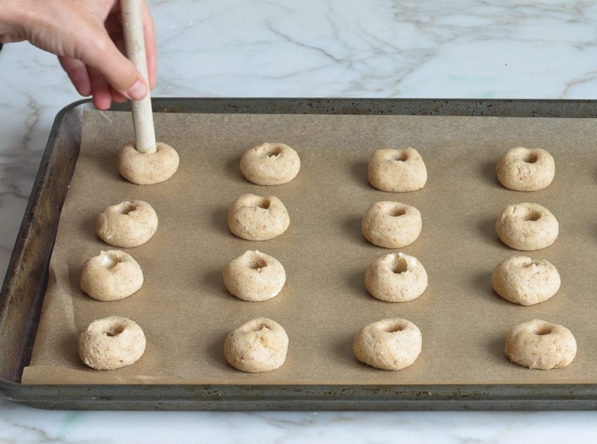 Person using a wooden spoon to make indents in balls of cookie dough.