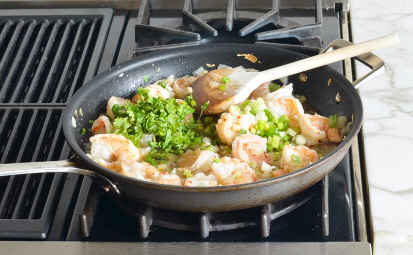 Scallions and cilantro in a skillet with shrimp.