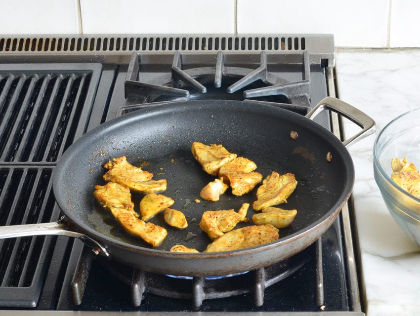 Chicken cooking in a skillet on a stovetop.