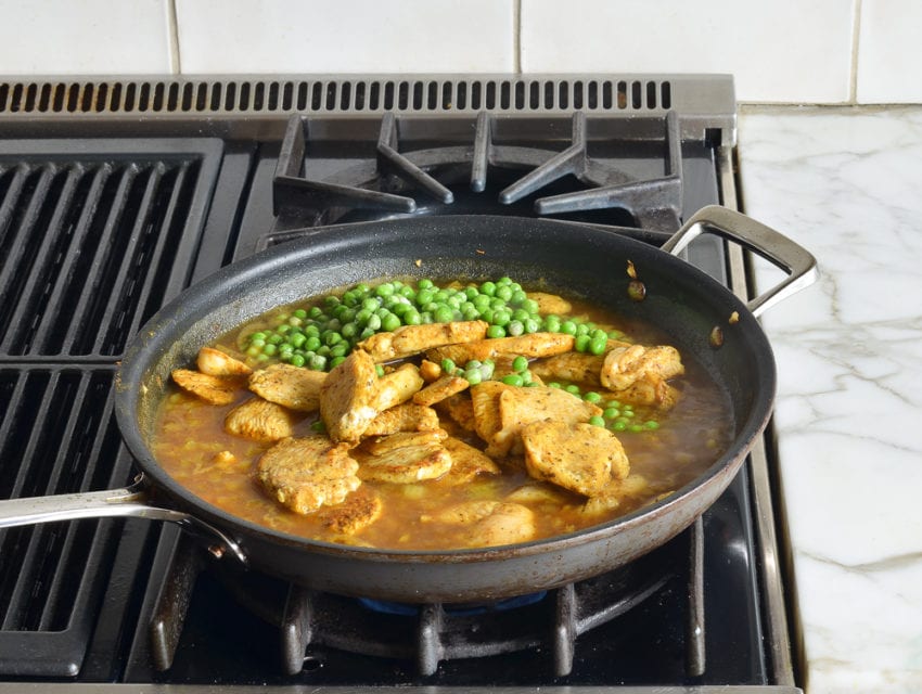 Chicken, peas, chicken stock, and other ingredients in a skillet.
